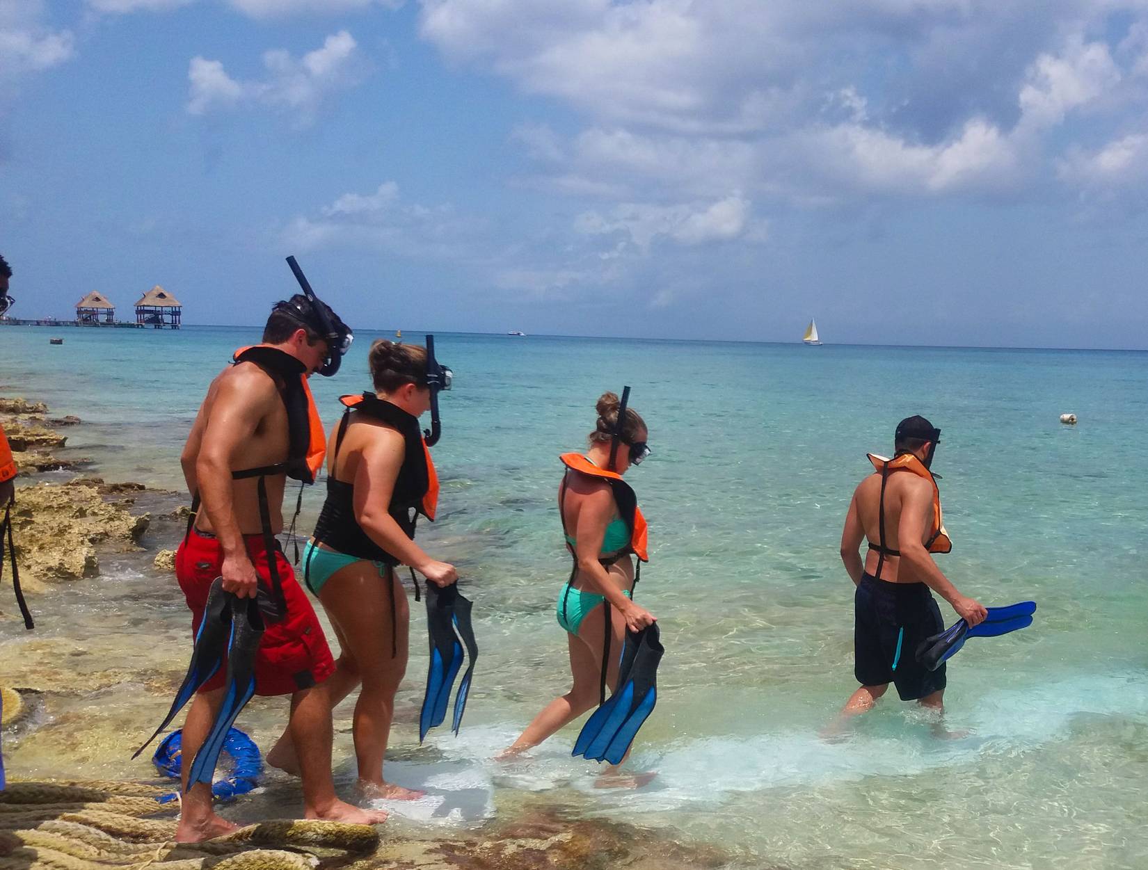 A group of friends wades into the water off a Cozumel beach to go snorkeling