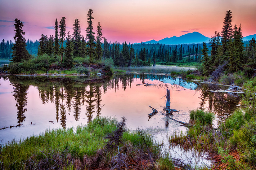A smoky haze hangs over the distant mountains as the sun sets over a lake in Wrangell-St Elias National Park, Alaska
