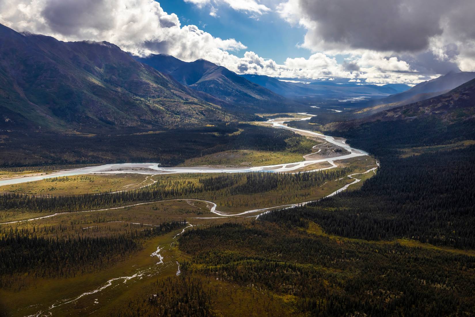 A river flows in a valley at Gates of the Arctic National Park and Preserve, Alaska, USA. The sky is cloudy and mountains can be seen on both sides of the river.