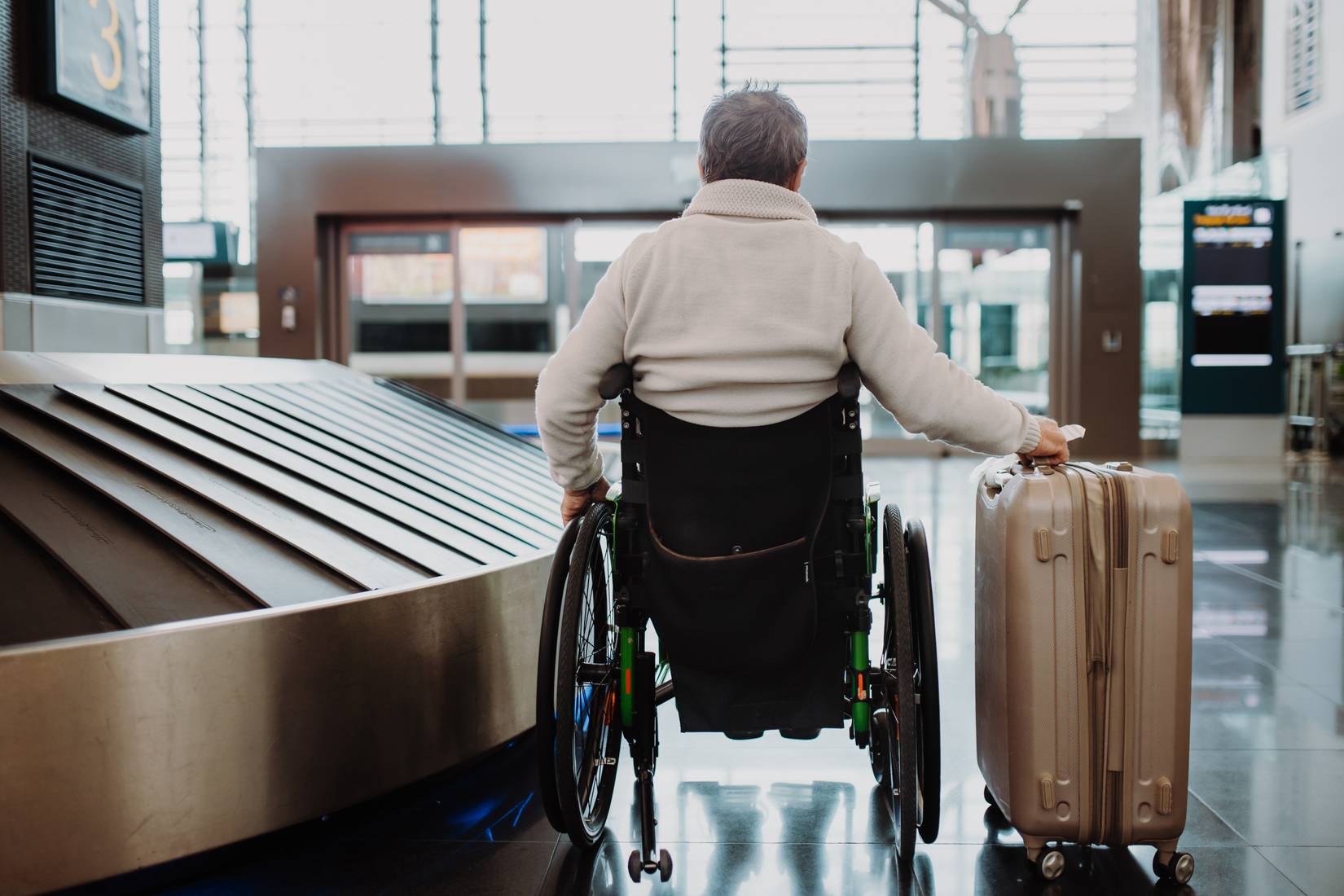 Rear view of man on wheelchair at airport with his luggage.