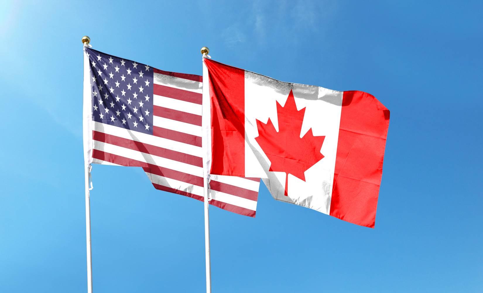 USA and Canada flags against cloudy sky