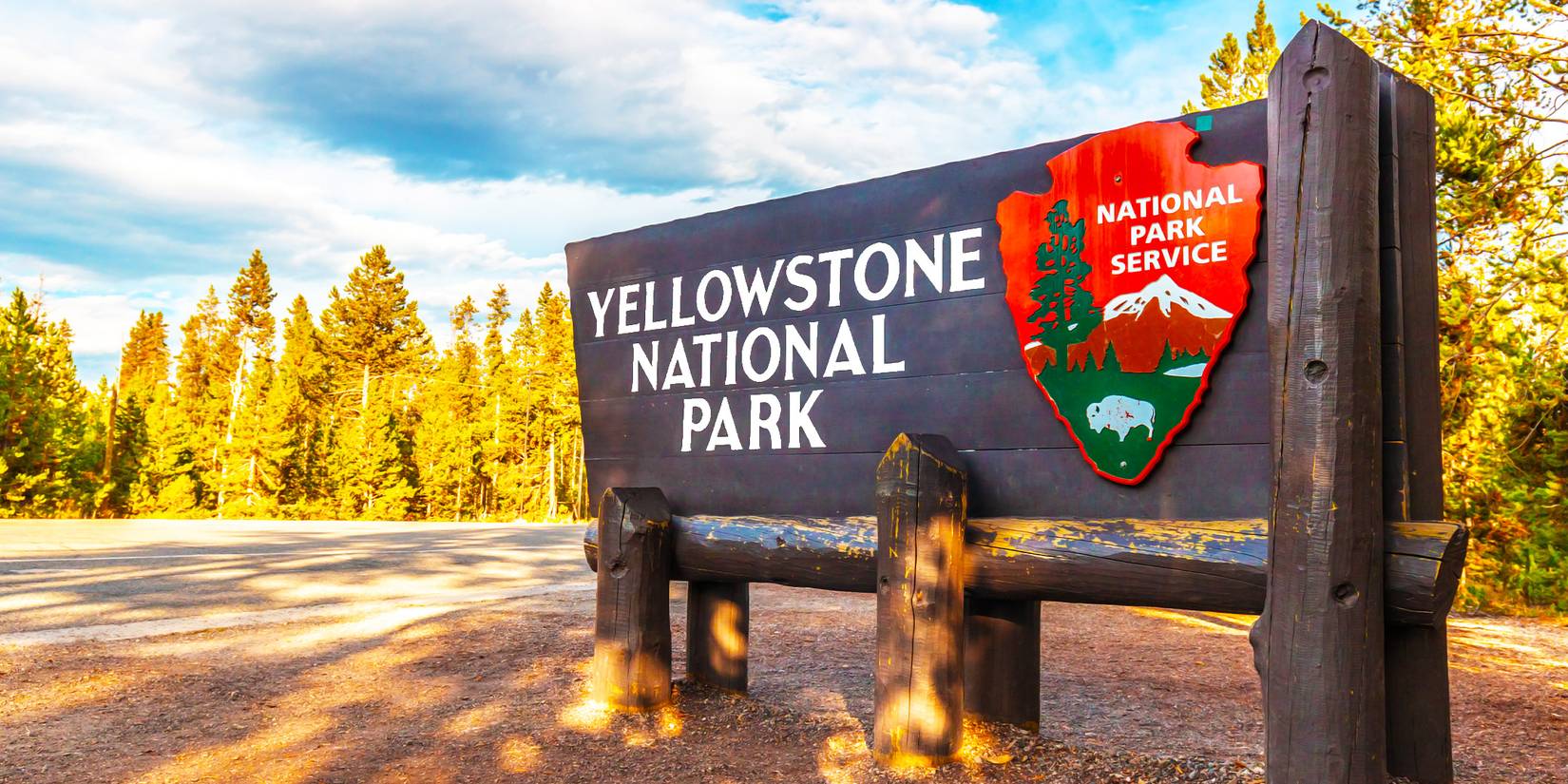 Entrance sign to Yellowstone National Park in front of a background of trees and cloudy sky