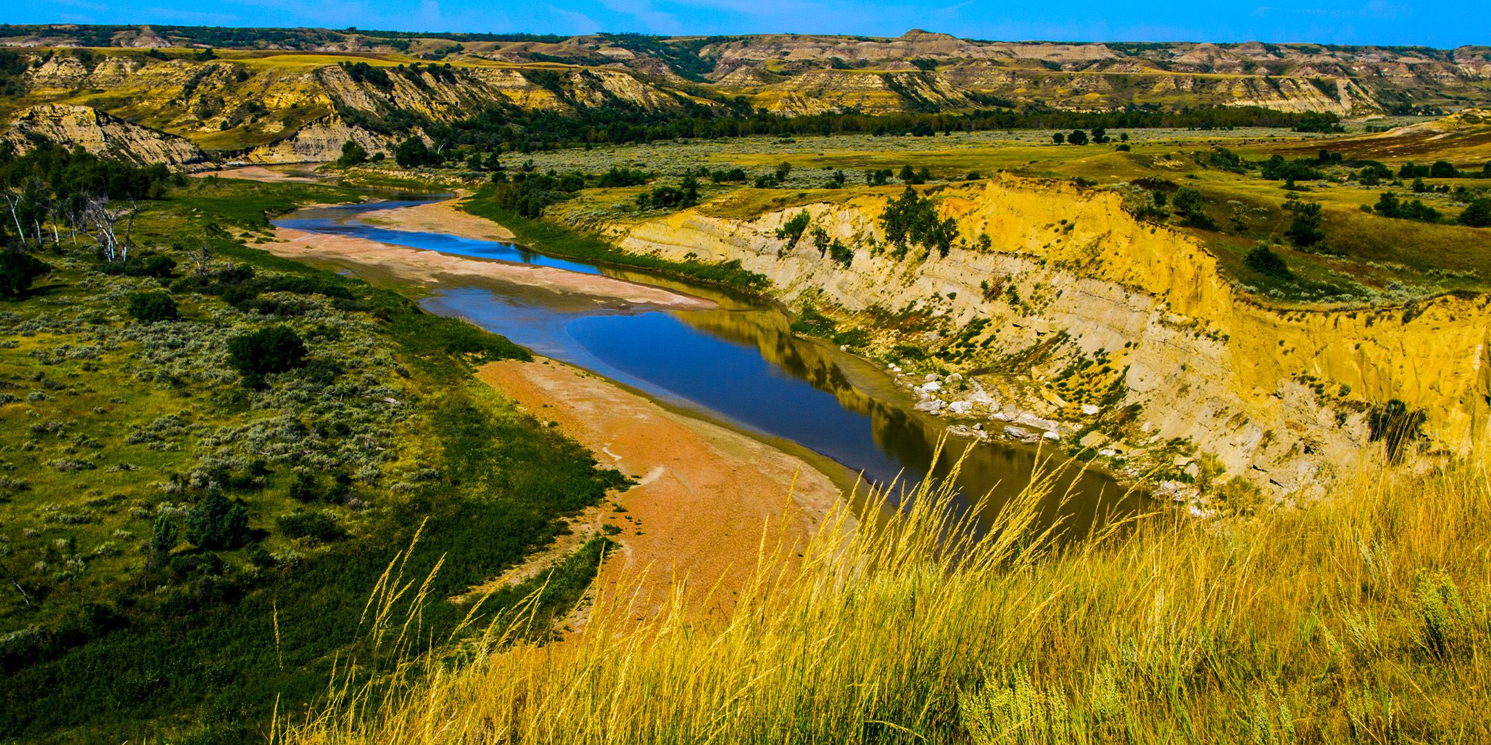 Green and yellow grass, cliffs in the distance, and a curving river on a clear day