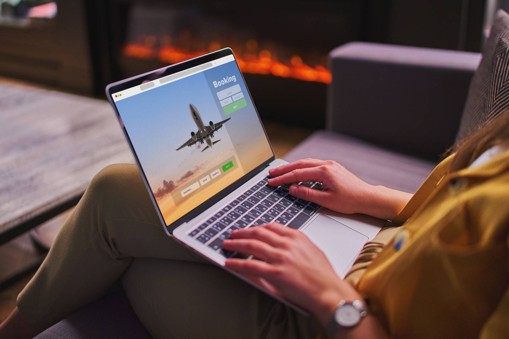 A woman booking flight tickets sitting near a fireplace.