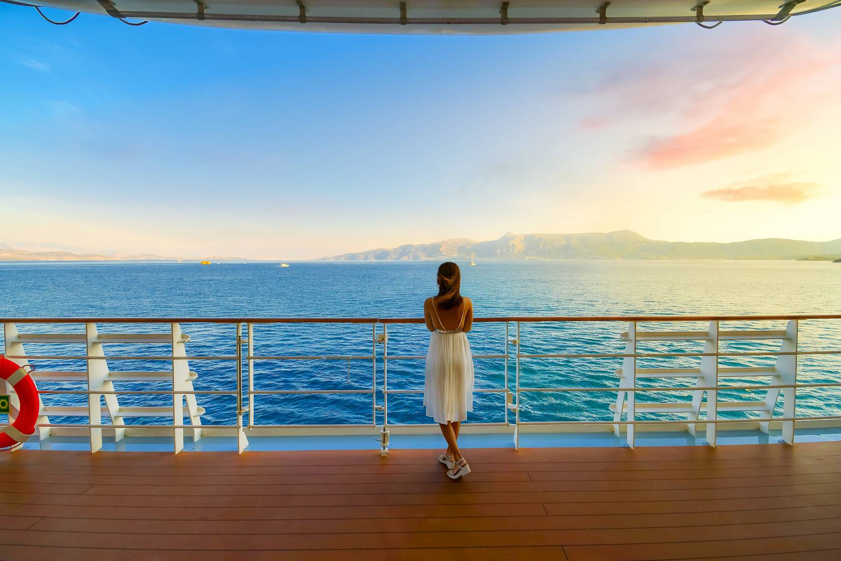 A woman stands on the deck of a cruise ship at sunset while it cruises the Mediterranean sea passing by Greek Islands near Corfu