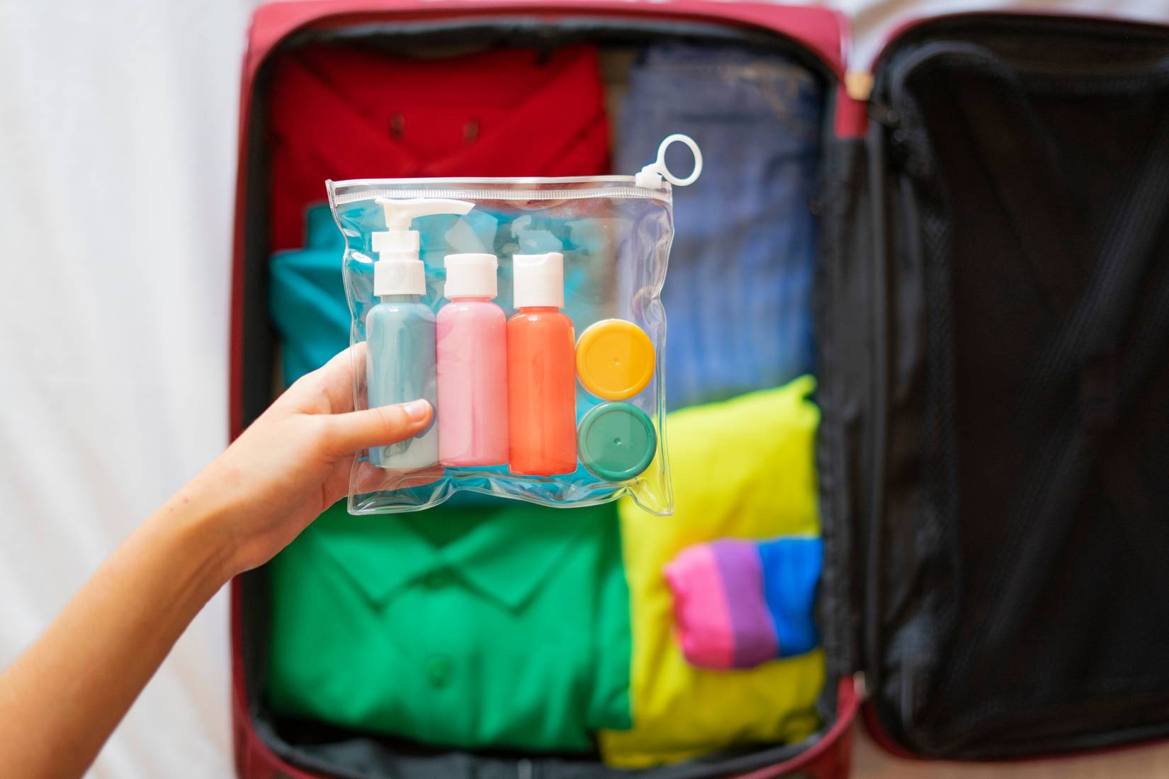 A tourist is putting a toiletry bag with liquids in the suitcase