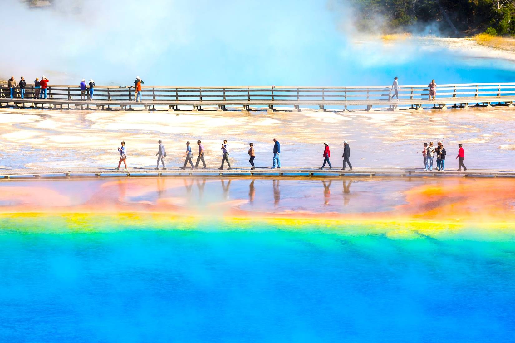 Tourists walk across the boardwalk by the Grand Prismatic Spring in Yellowstone National Park