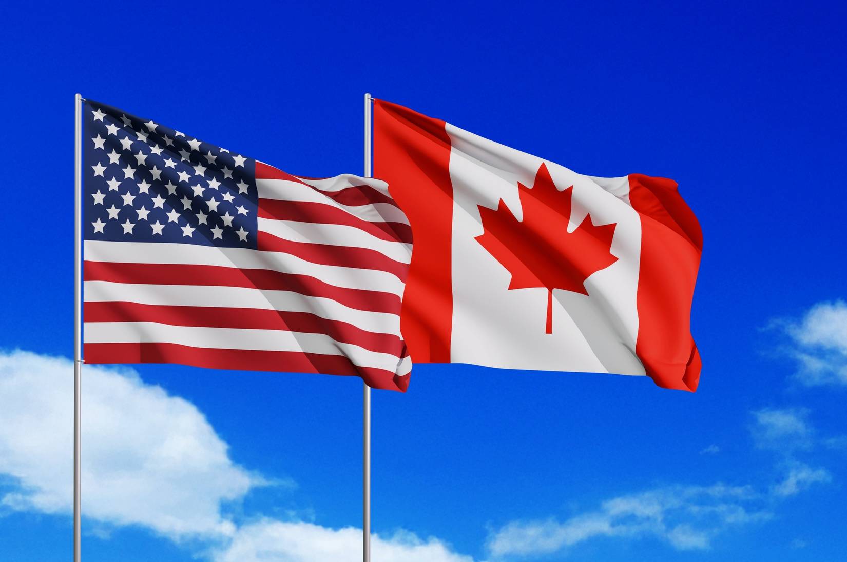Canadian and USA flags flying under a clear blue sunny sky