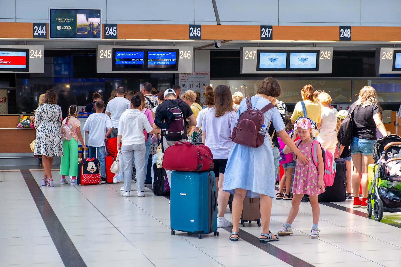 Tourists stand with luggage and children in line at an airport terminal