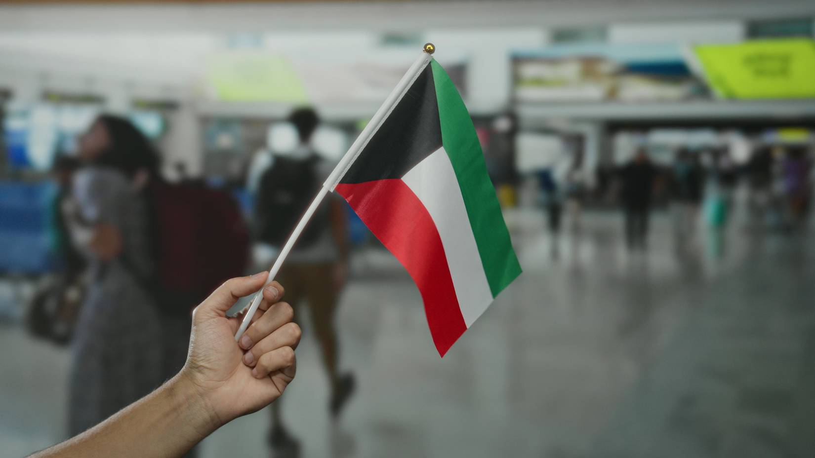 Man holding a Kuwait flag inside a busy airport terminal with people in the background