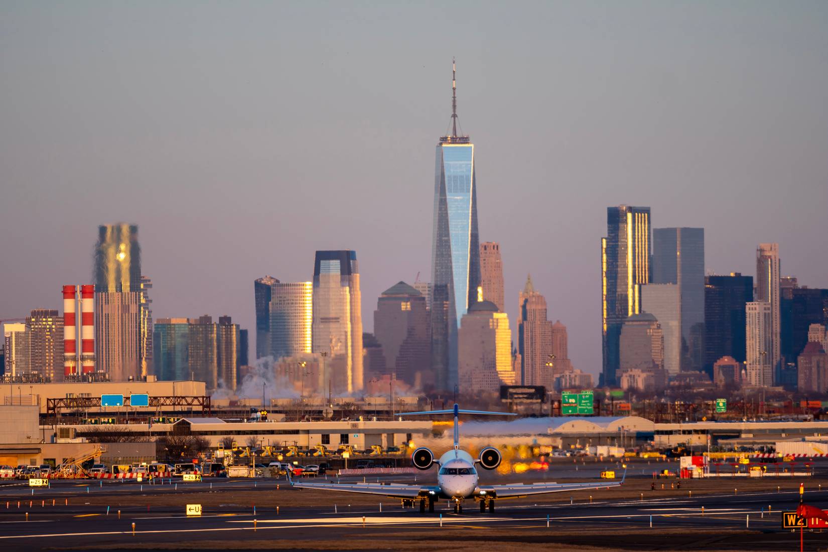 A plane taxis down the runway at Newark Liberty International Airport in New Jersey at dusk, with lower Manhattan's skyscrapers in the background.
