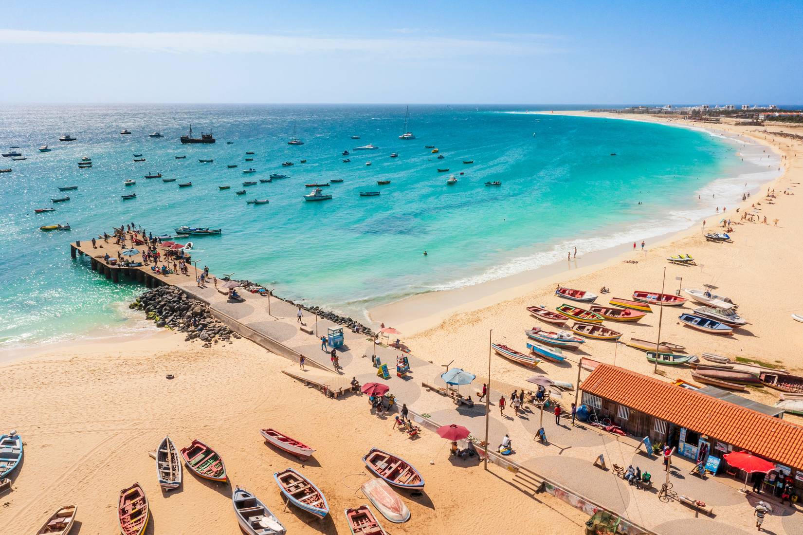 People on the beach pier, with boats on the turquoise water in the city of Santa Maria, Sal, Cape Verde