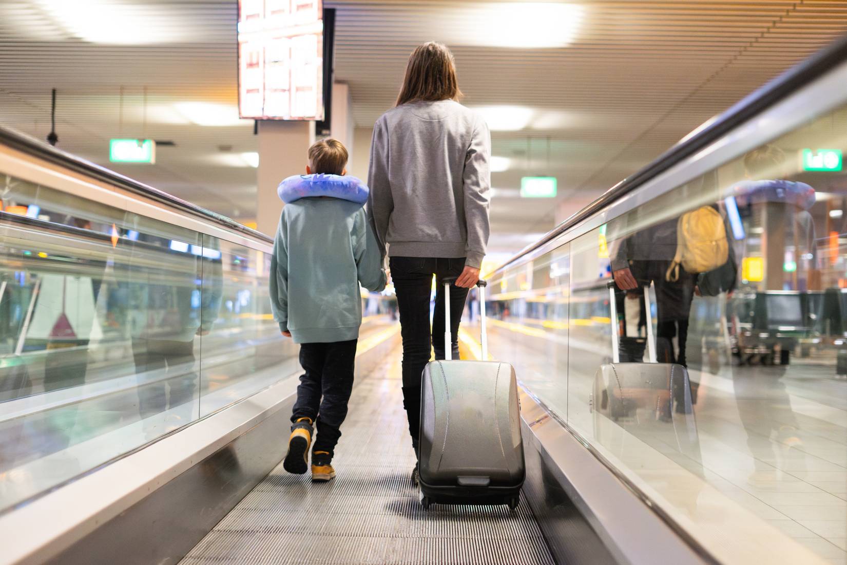 A mother and child walking through the airport with luggage towards the departure gate