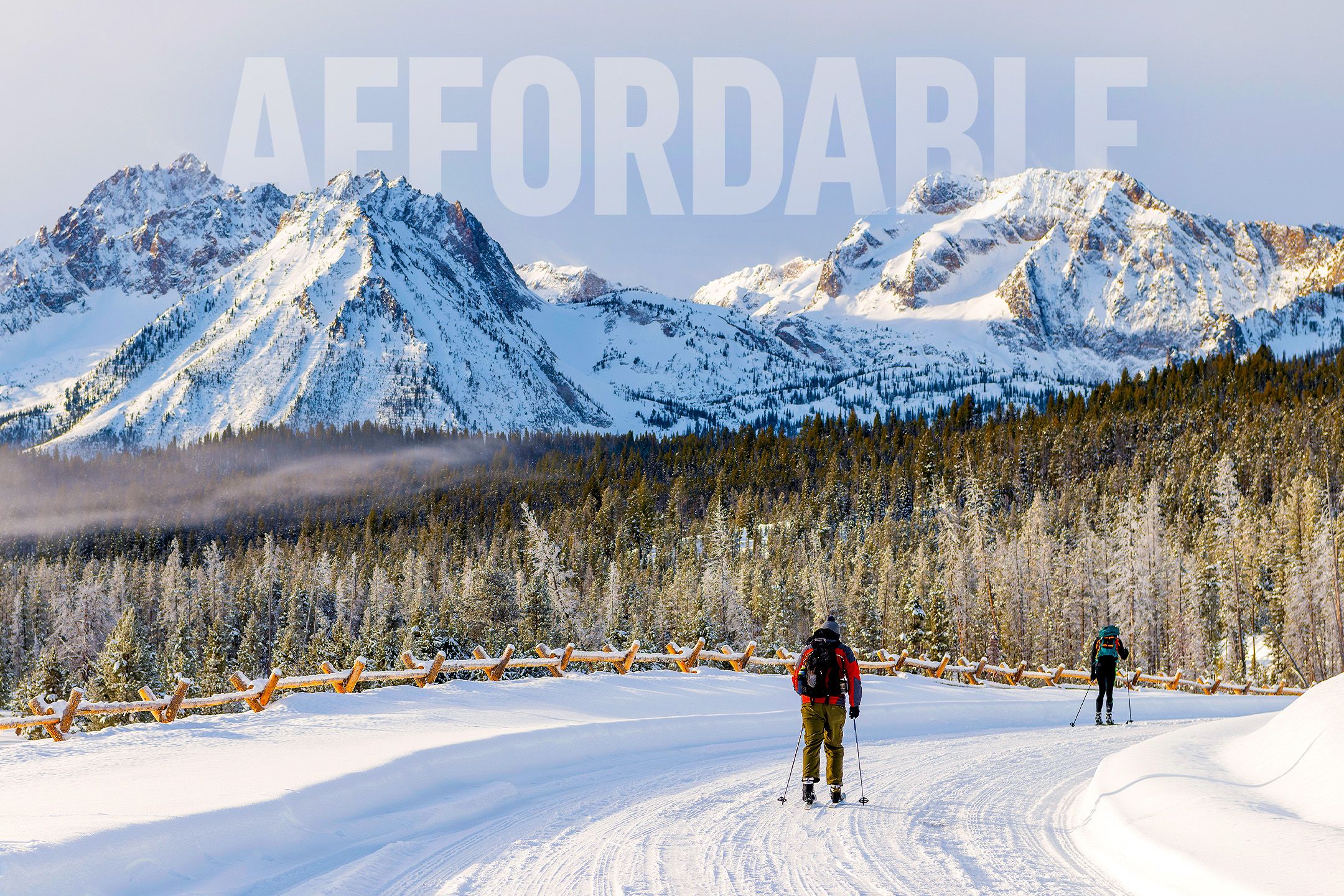 Two skiers in the snow on a ski trail with evergreen forests and the Sawtooth Mountains in the distance