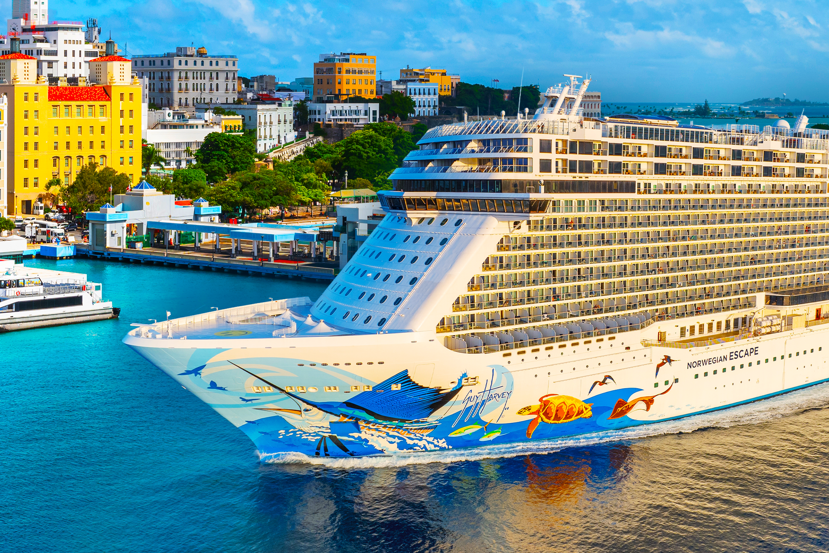 Norwegian cruise in the foreground, blue water, pier and colorful buildings in the background, on a cloudy day
