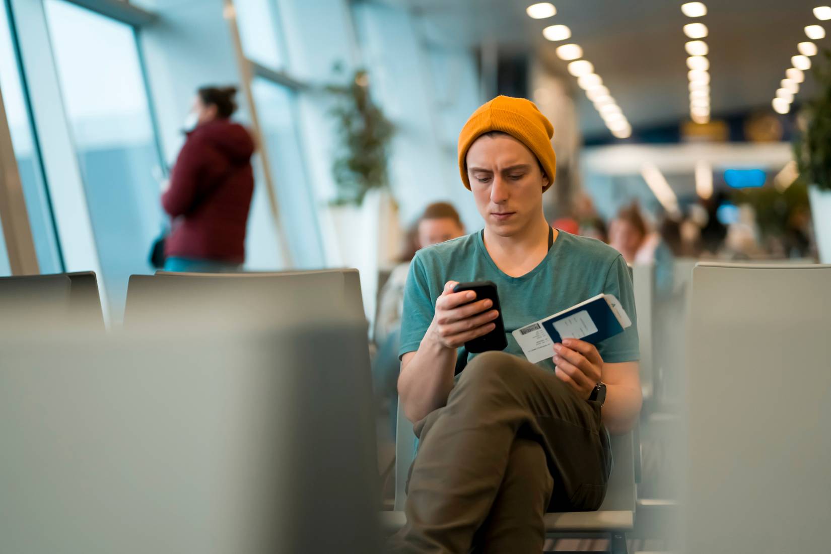 A man sits at the airport and checks in for the next flight via an app on his phone, waits for the plane and works while traveling.