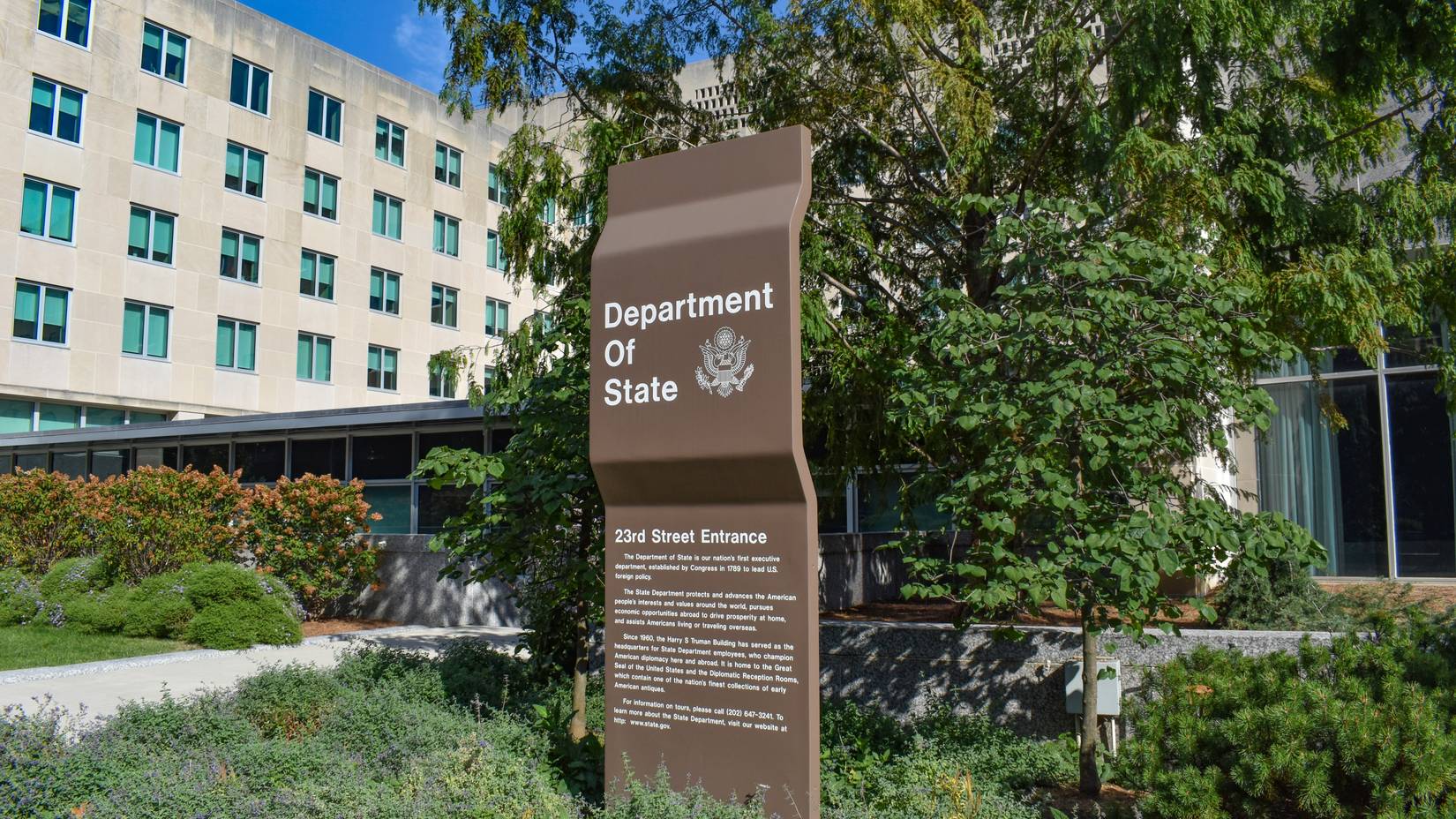 U.S. Department of State sign for the 23rd Street entrance with the State Department Building in the background