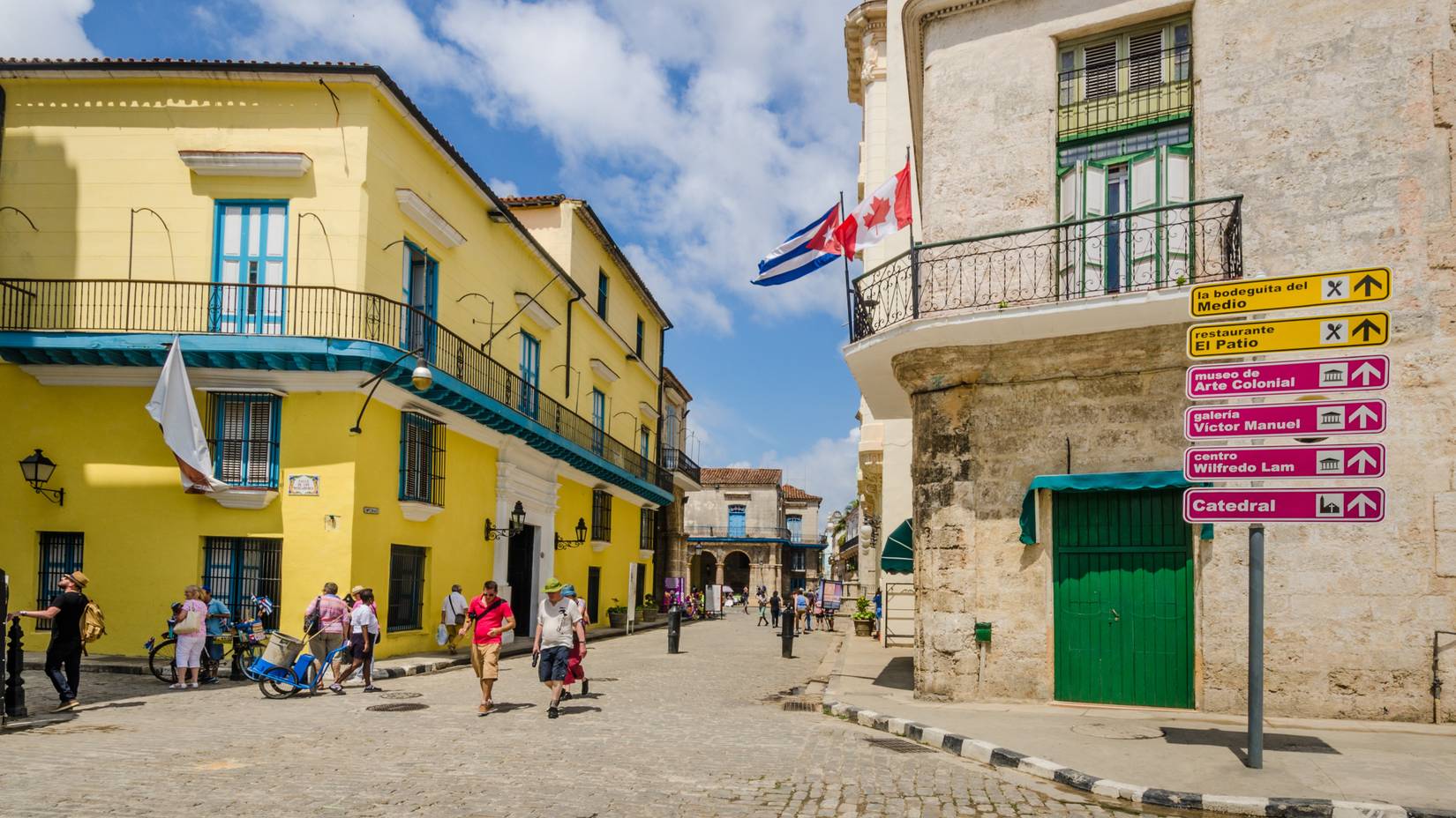 Tourists walking as Cuban and Canadian flags fly from one of the buildings on the corner of Mercaderes and Emperado in the Plaza de la Catedral district in Havana, Cuba