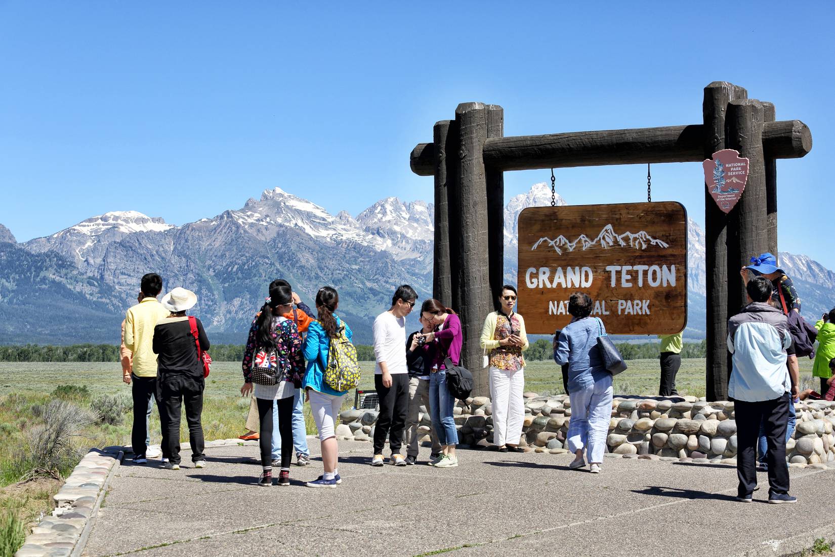 A group of adult tourists pose for pictures at the entrance sign for Grand Teton National Park near Jackson Wyoming. 