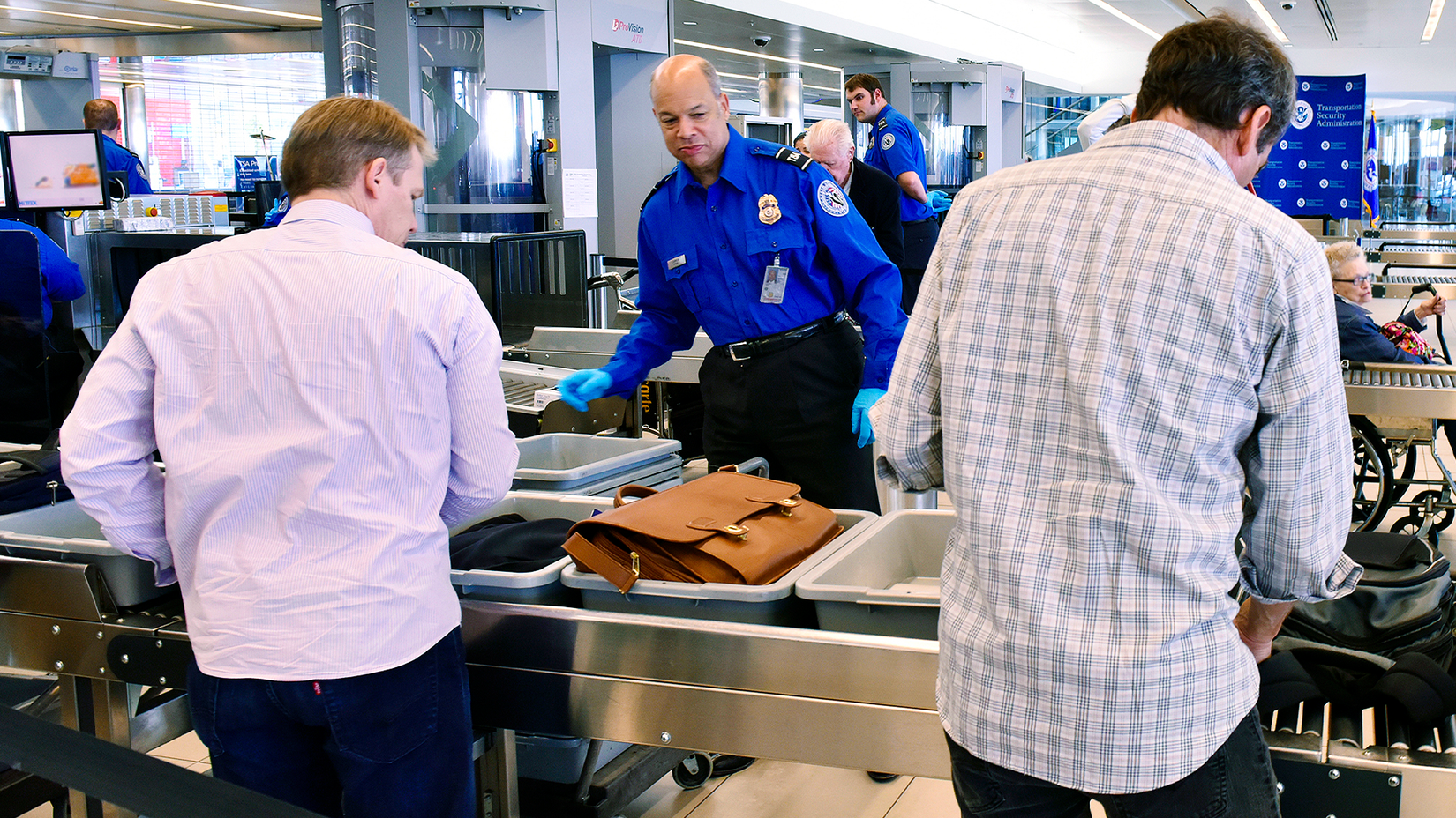 TSA agent helping two passengers place items in grey trays to go through TSA scanner at airport