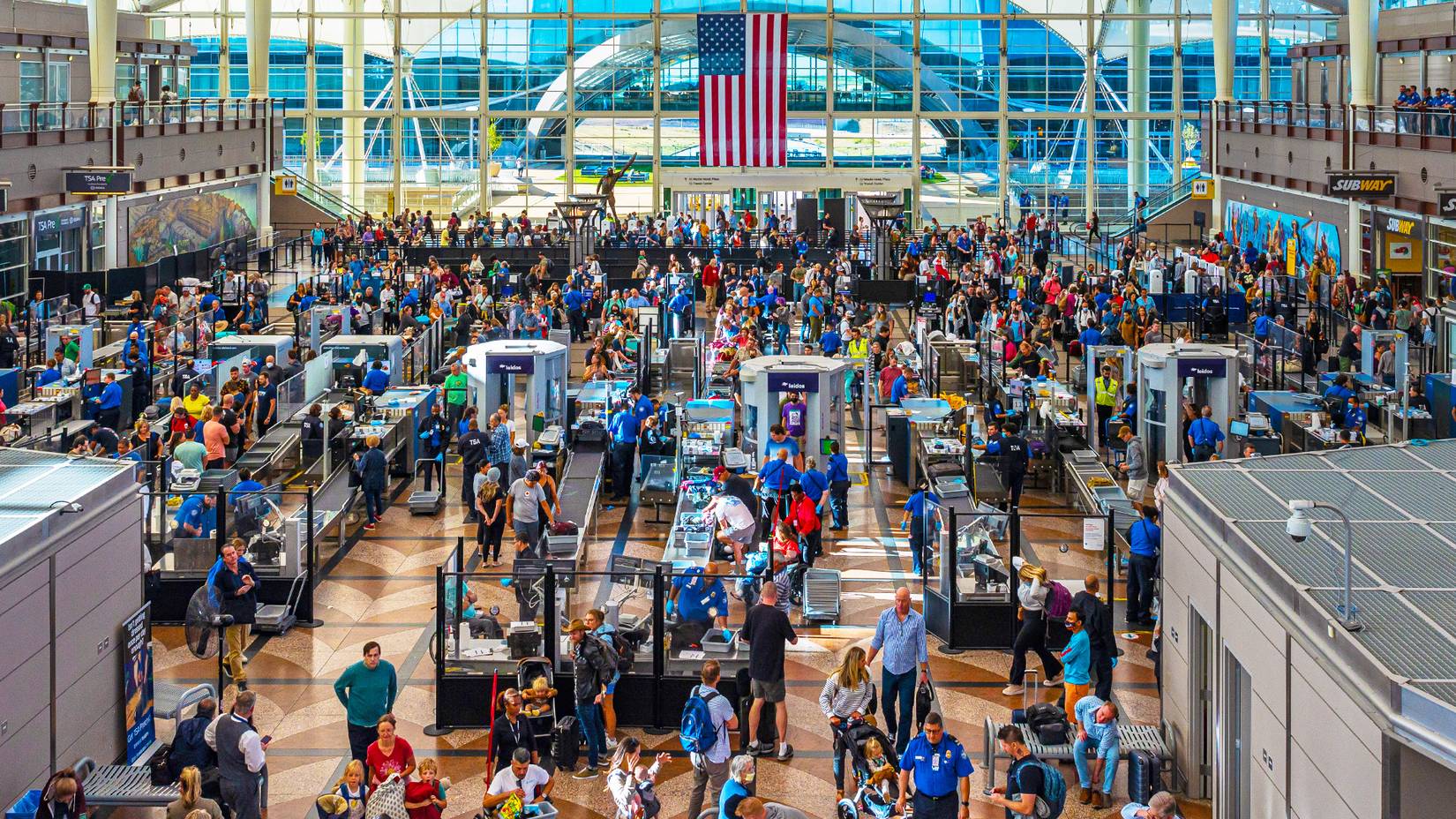A very crowded, long line at the TSA Chicago Airport with an American flag hanging from the window