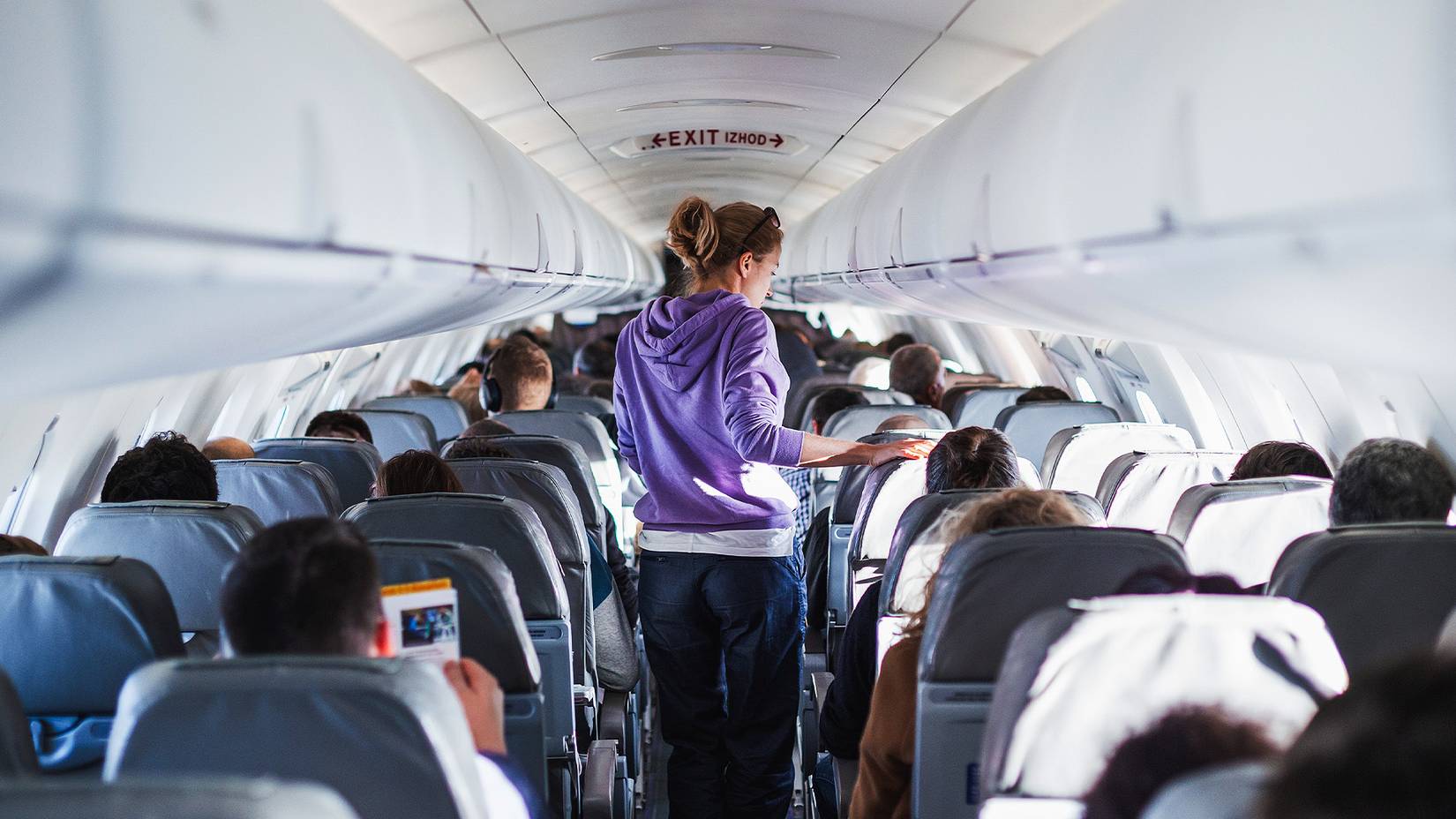 Passenger in a purple sweater walking down the central aisle of a plane cabin full of travelers