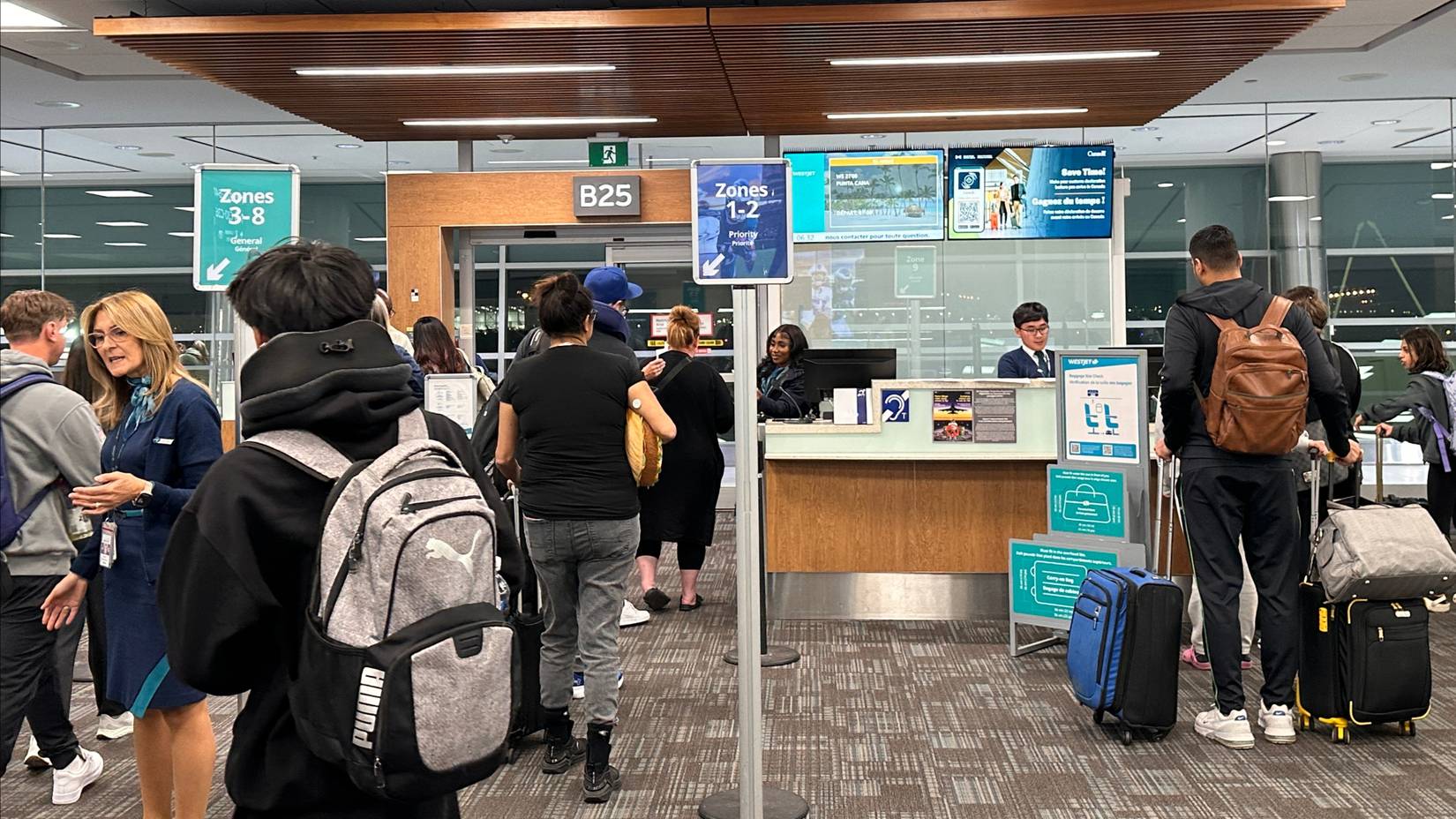 Westjet passengers line at the boarding gate with their luggage and backpacks at Toronto Pearson Airport