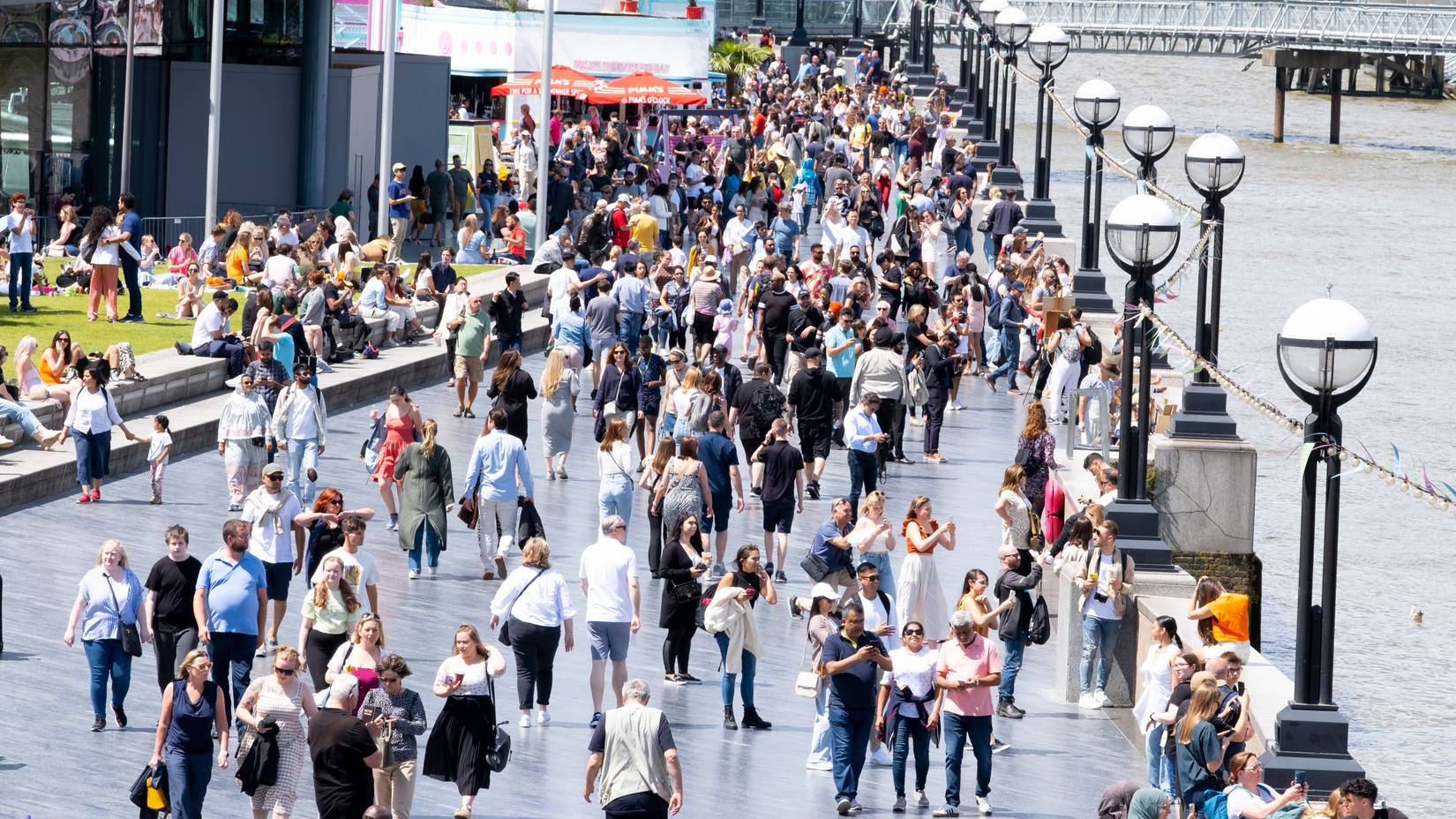 The Queen's Walk on the south bank of the River Thames near Tower Bridge, London, packed with foreign tourists and sightseers enjoying the walk along the promenade.