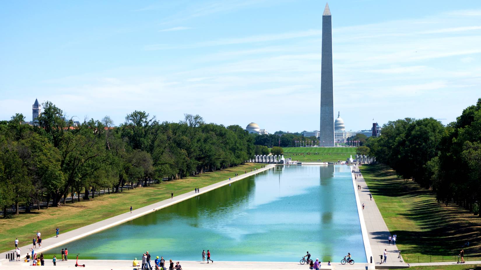 The reflection of the Washington Monument on the Lincoln Memorial Reflecting Pool, with people walking on the poolside 