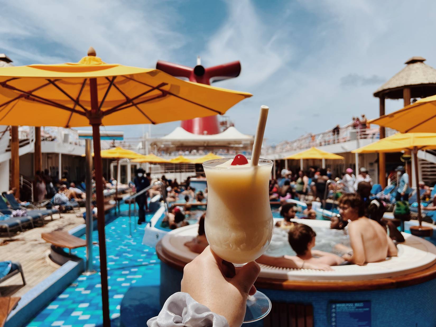 Passenger holding a Pina Colada frozen cocktail on Carnival Cruise Line by the pool.