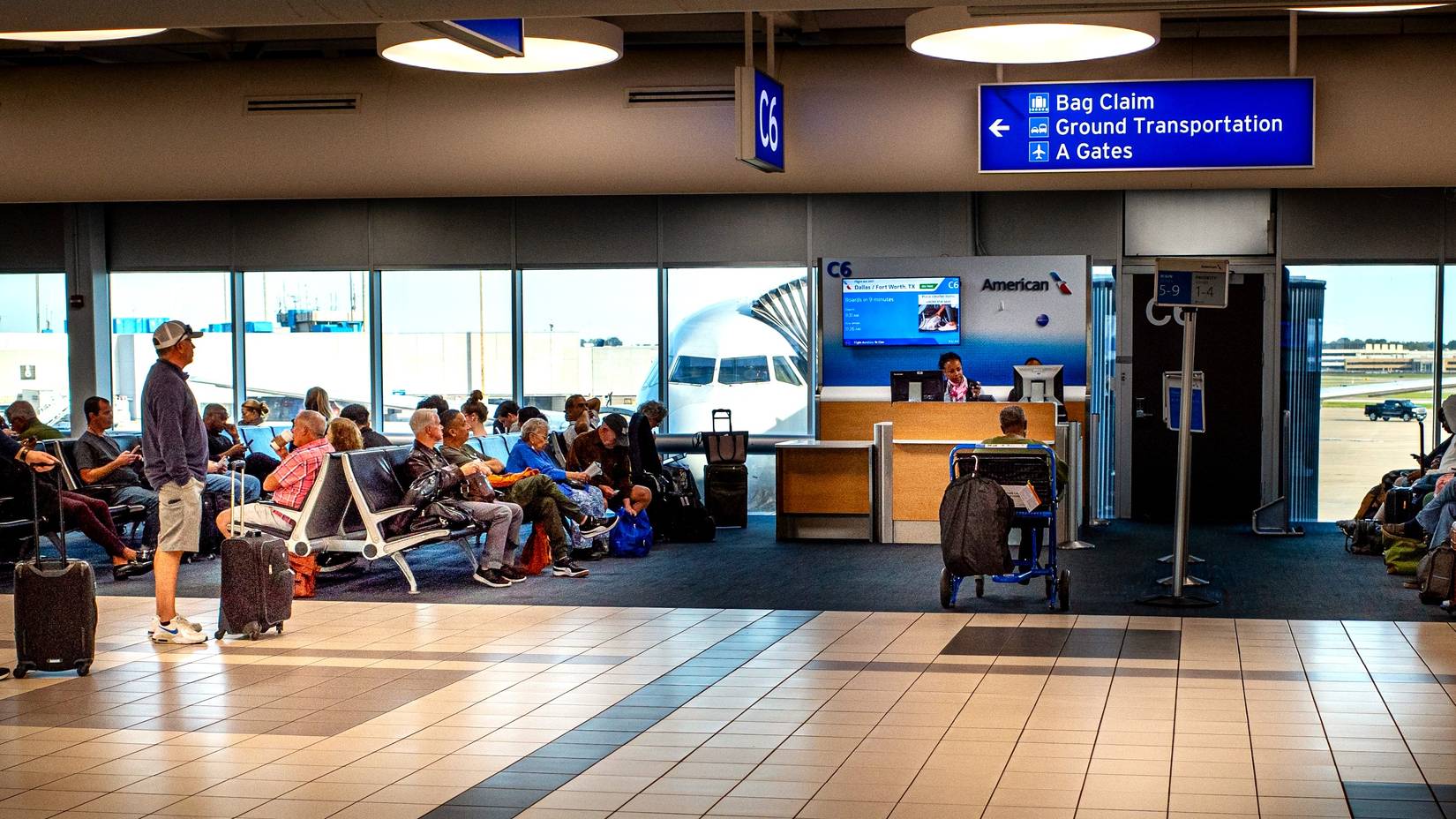 Passengers wait to board an American Airlines flight at a gate in Lamber Field airport