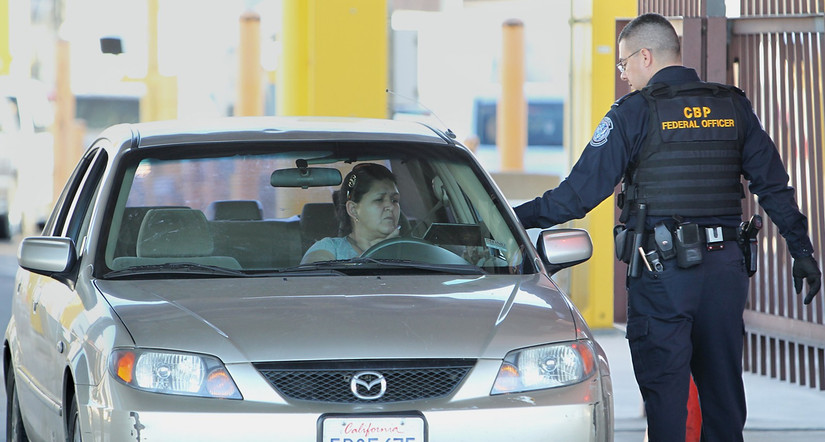 U.S. Customs and Border Protection (CBP) officer checking a traveler's vehicle at the US border