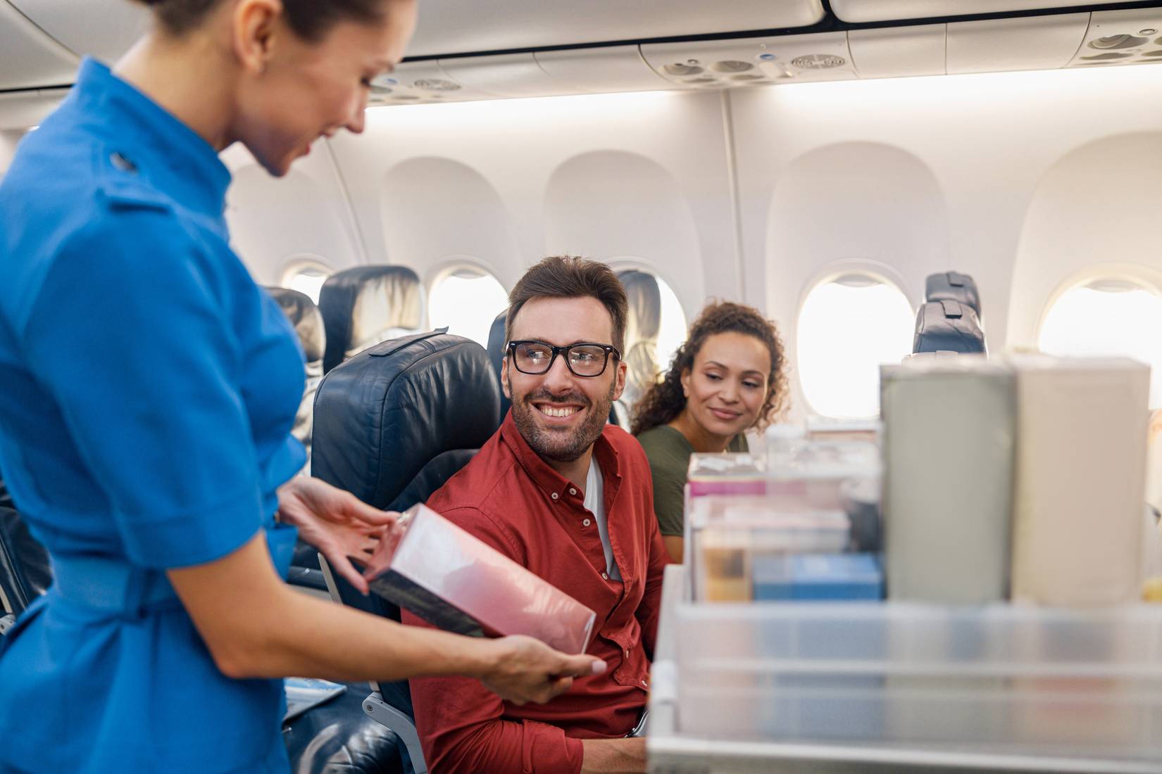 Smiling stewardess offering products or gifts to buy to passengers on aircraft