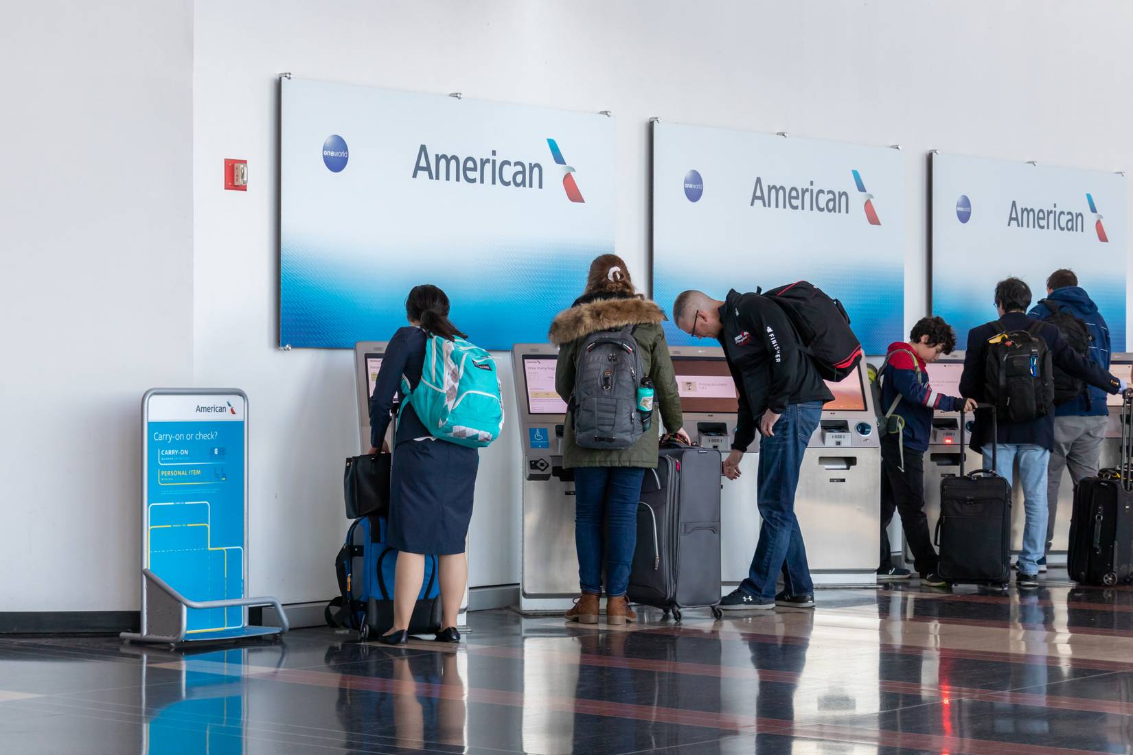 American Airlines passengers at a U.S. airport's check-in area, utilizing a self-service baggage drop