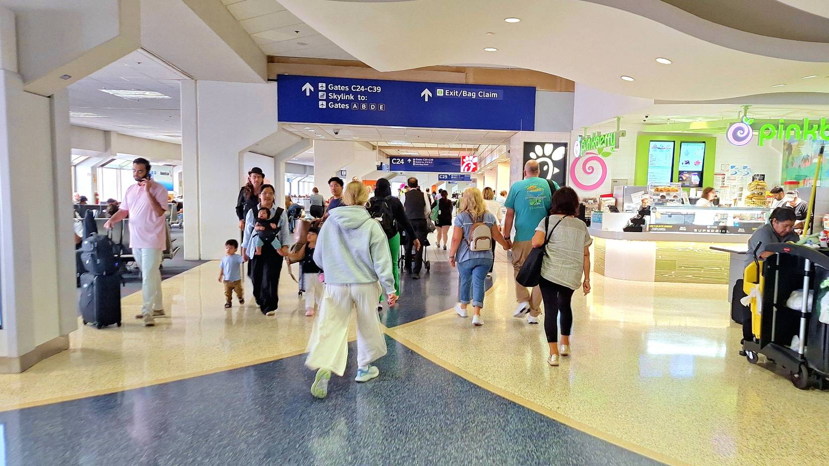 People walk through a busy terminal at Dallas-Fort Worth International Airport past shops and directional signs