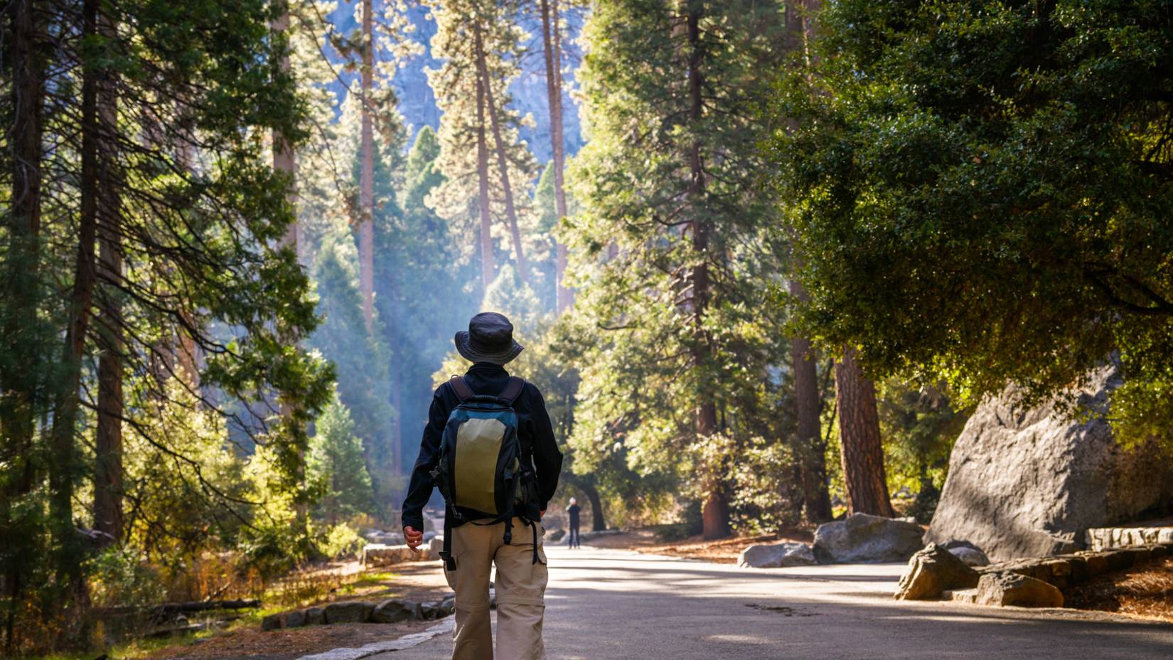 Man hiking the Lower Yosemite Fall trail, surrounded by trees, in Yosemite National Park, California