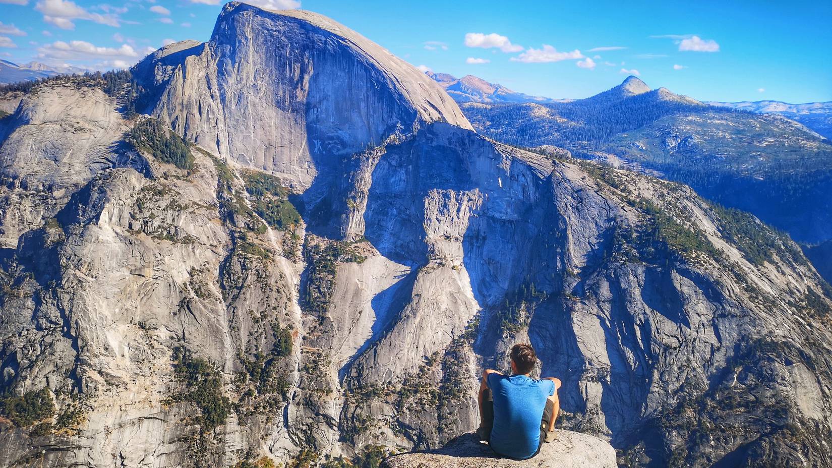 Man looks out at Half Dome from the summit of North Dome, Yosemite, California, USA