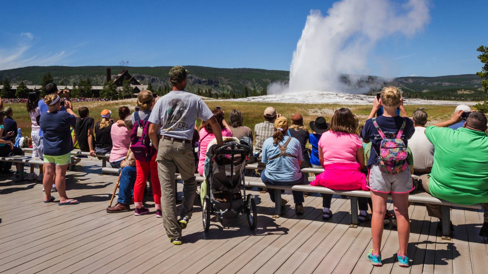 Group of tourists standing watching Old Faithful Geyser in Yellowstone National Park, Wyoming