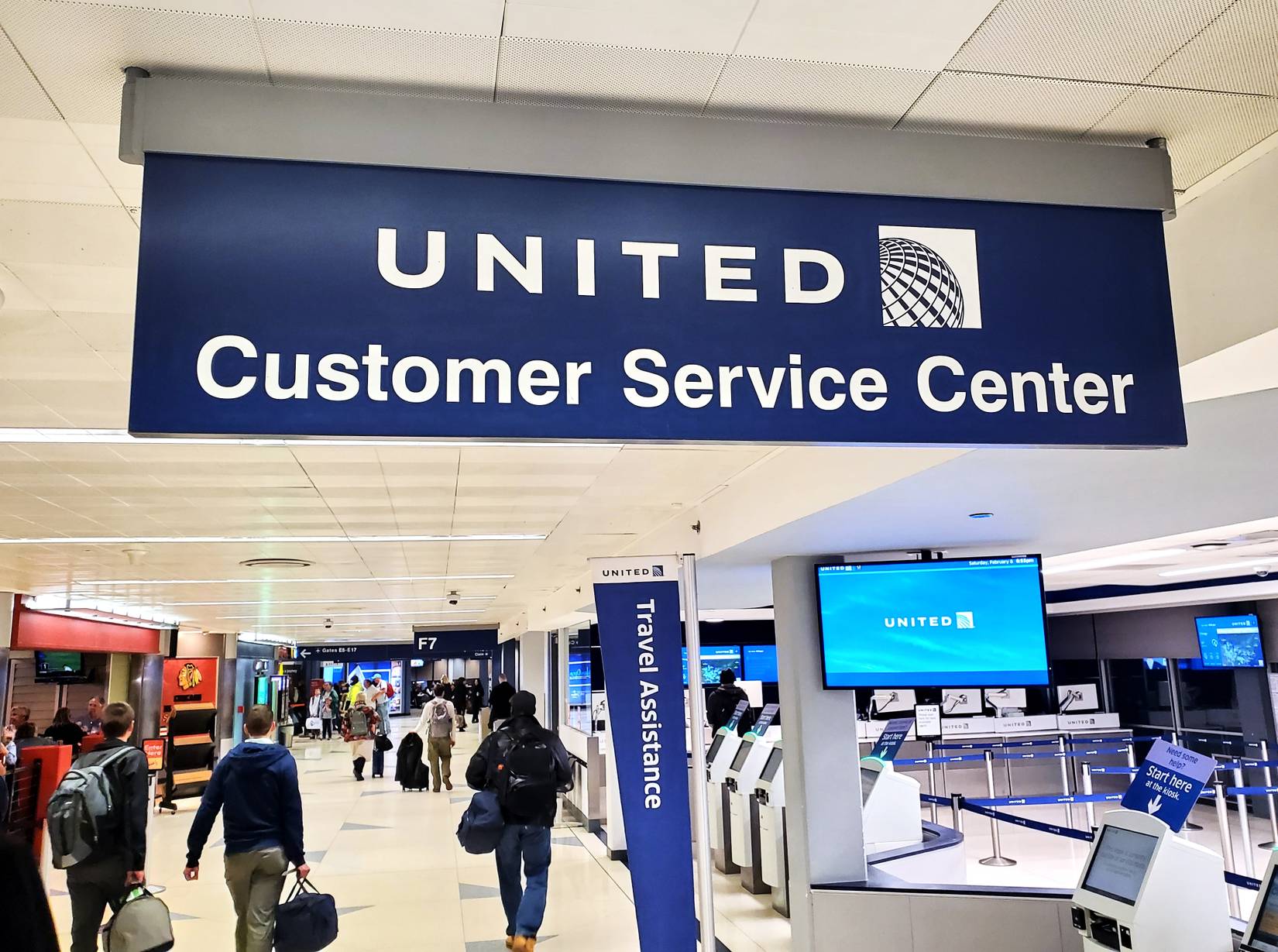 Passengers walk towards the United Customer Service Center within an airport terminal.