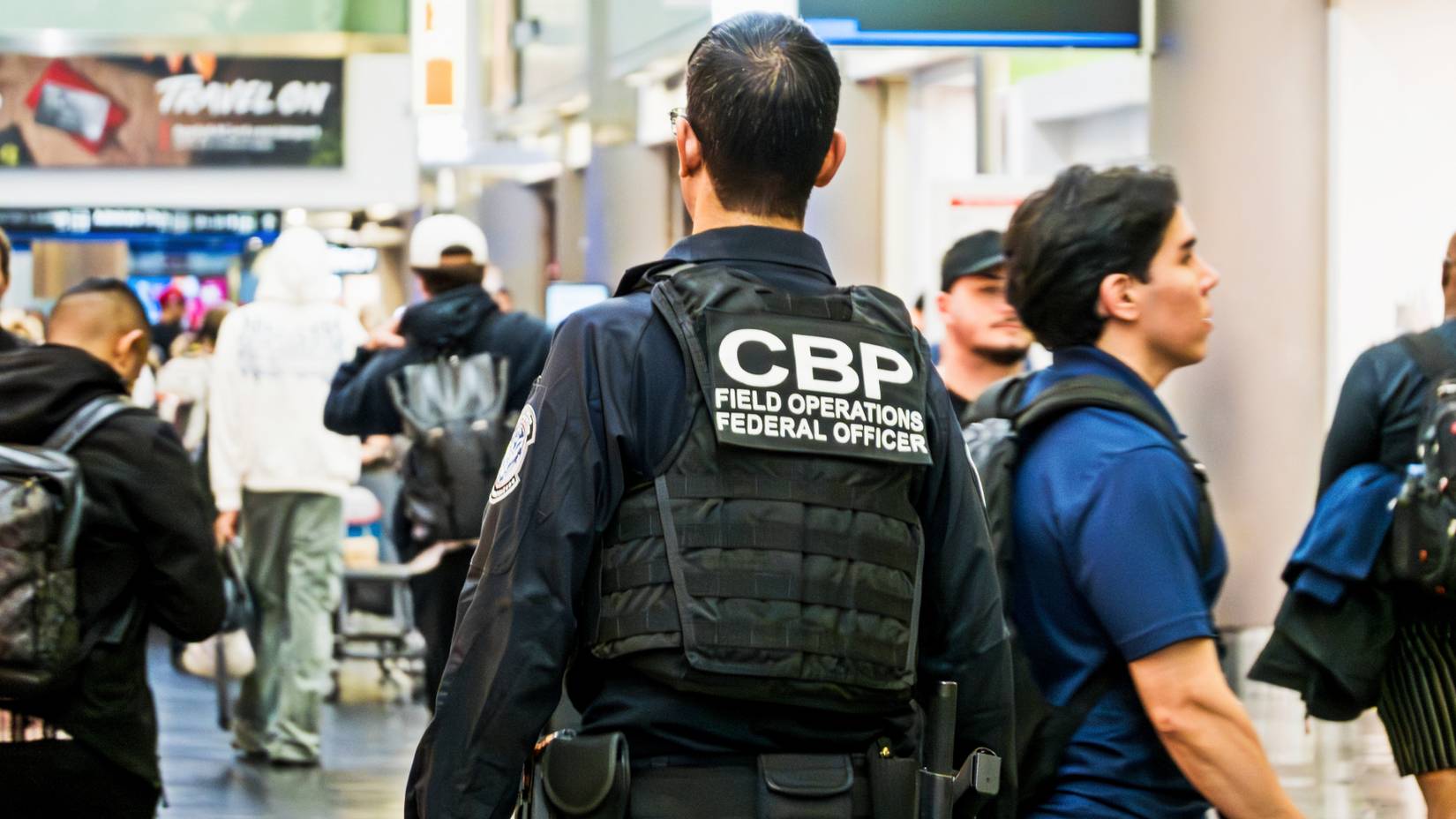 U.S. Customs and Border Protection (CBP) officer walks through a busy airport terminal concourse with travelers