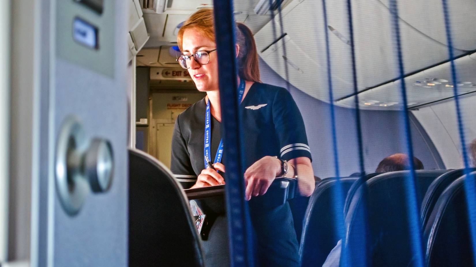 United Airlines flight attendant helping passengers in first class on an airplane mid-flight